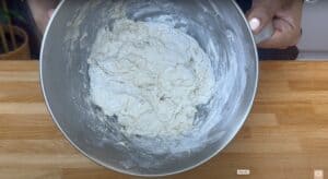 Bowl of bread dough being mixed by hand on a wooden countertop. Perfect for baking recipe content.